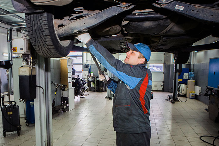 Механік оглядає автомобіль знизу на підйомнику — перевірка підвіски і гальм перед купівлею вживаного авто